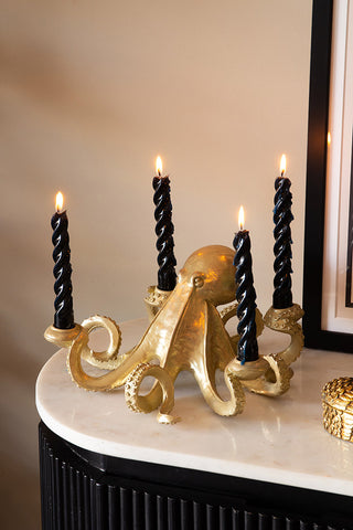 The Gold Octopus Candlestick Holder with four lit candles, displayed on a marble sideboard with some other home accessories.