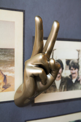 The Gold Peace Hand Wall Art & Coat Hook displayed on a wall with printed wallpaper.