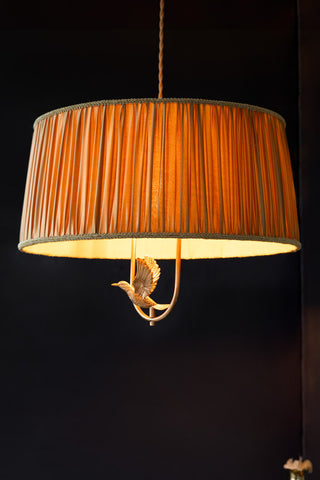 The Gold Ruched Hanging Bird Pendant Light shown with the light on against a black wall. 