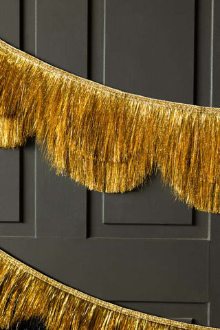 The Gold Scalloped Tinsel Garland styled on a black panelled wall.