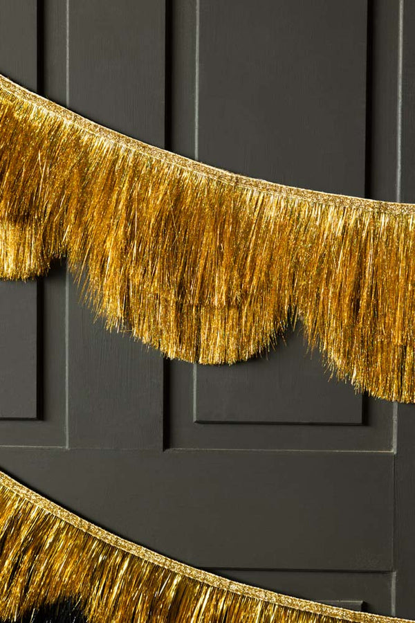 The Gold Scalloped Tinsel Garland styled on a black panelled wall.