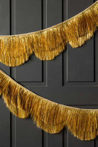 The Gold Scalloped Tinsel Garland styled draped across a black panelled wall.