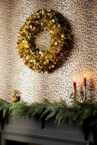The Gold Tinsel Sparkle Christmas Wreath, shown on a leopard print wall above a fireplace. 