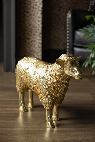 The Gold Sheep Decorative Ornament styled on wooden floor with an armchair and a plant in the background.