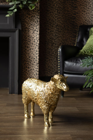 The Gold Sheep Decorative Ornament displayed on a wooden floor, with some plants and an armchair in the background.