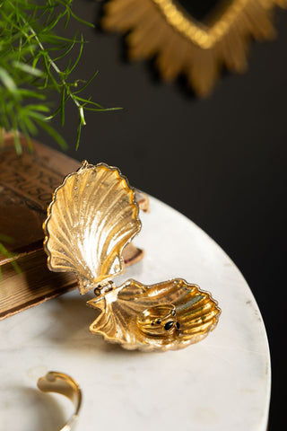 A Gold Shell Trinket Dish styled with a ring on, displayed on a table with a book and some other accessories.