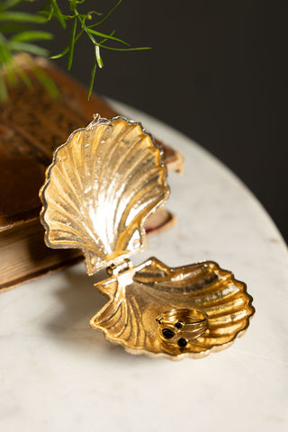 Close-up of the Gold Shell Trinket Dish with a ring inside, styled on a white surface with a book and plant.