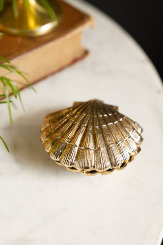 The Gold Shell Trinket Dish closed and on a white surface with some accessories in the background.