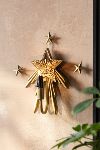 The Gold Star Candle Wall Sconce shown on a plaster wall with  black dinner candle. 