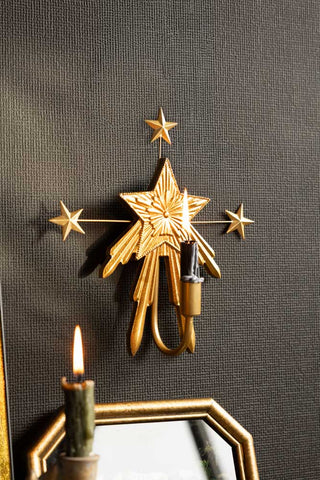 The Gold Star Candle Wall Sconce, shown on a black wall with a black dinner cande.