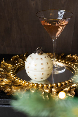 The Gold Star Christmas Candle Bauble Ornament with the lid on, styled on a gold mirror with a cocktail glass.