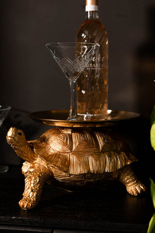 The Gold Tortoise With Tray displayed with a cocktail glass and wine bottle on, on a dark surface.