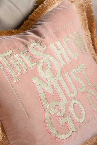 A detail image of the Pink Velvet Double-Fringed Show Must Go On Embroidered Cushion showing the gold lettering.