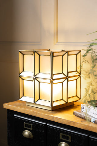 The Gold Geometric Glass Table Lamp shown with the light on on a apothecary-style console table. 