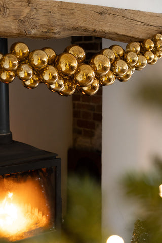 The Gold Antique-Effect Bauble Christmas Garland styled on a fireplace above a lit log burner.