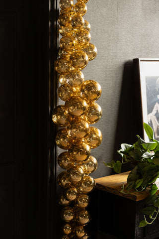 The Gold Antique-Effect Bauble Christmas Garland displayed hanging in forn tof a black wall, next to a table with an art print and a plant on.