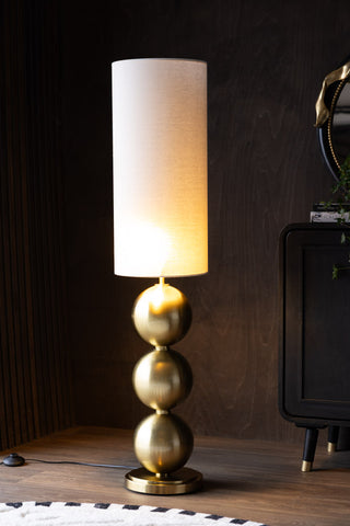 The Golden Balls Floor Lamp switched on and styled next to a rug and sideboard with accessories on.