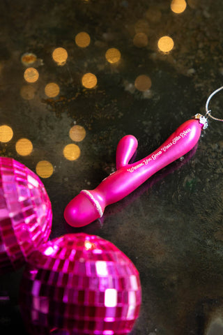 The Good Vibes Sex Toy Christmas Tree Decoration on a darksurface with some pink disco balls.