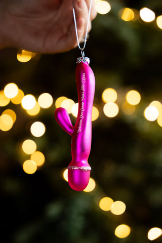 The Good Vibes Sex Toy Christmas Tree Decoration being helf up in front of some fairy lights.
