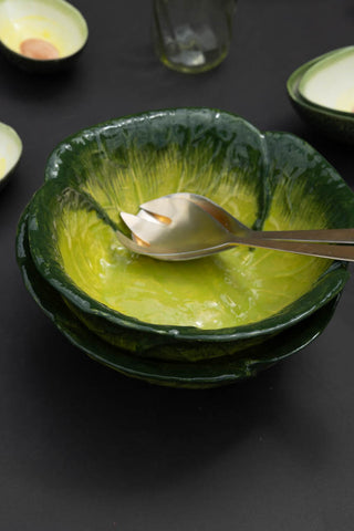 Closer image of the green cabbage bowl on a dark table with serving spoons