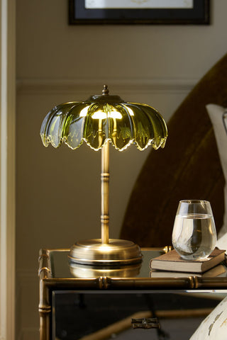 Lifestyle image of the Gold & Green Desert Table Lamp displayed illuminated on a mirrored side table with a book and a drinking glass
