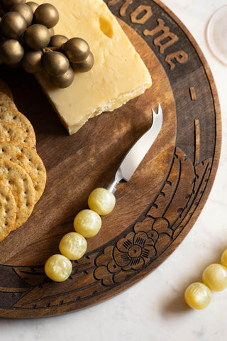 One of the HKLIVING Yellow Bobble Cheese Knives shown on a bread board with cheese and crackers. 