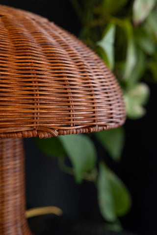 Detail image of the HKliving Rattan Toadstool Table Lamp with a dark wall and plant in the background. 