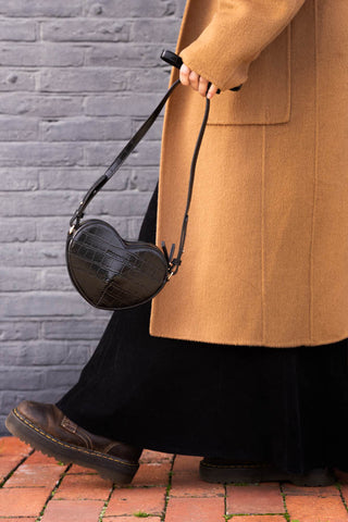 A black heart-shaped bag being held by a model walking outside.