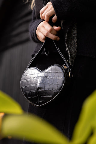 A black heart-shaped bag being held by a model in both hands.