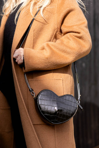 A black heart shaped bag being worn on a model's shoulder.
