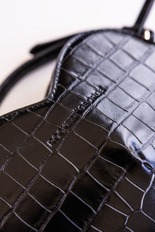 Close-up of the Rockett St George logo and croc-effect on a black heart-shaped bag.