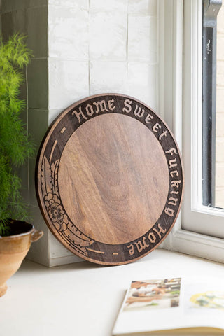 The Home Sweet Fucking Home Wooden Serving Board shown in a kitchen by the window against white zellige-style tiles. 