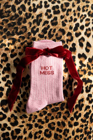 The Hot Mess Pink Glitter Socks shown with a red bow against a leopard print background. 