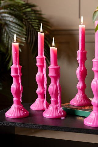 Lifestyle image showing a group of the Hot Pink Candlestick Shaped Candles in medium and tall, with leafy palms in the background.