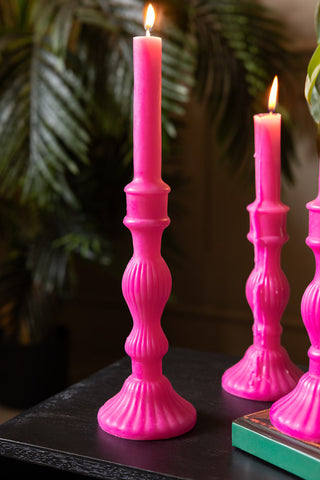 Image of the Hot Pink Candlestick-Shaped Candle - Tall shown with plants in the background, and the medium size candle can also be seen in the background. 