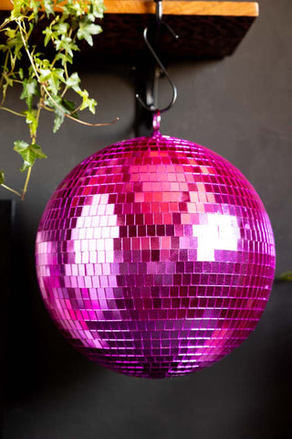 The Hot Pink Disco Ball hanging from a shelf, next to some greenery.