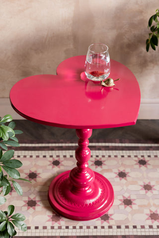 The Hot Pink Heart Metal Side Table shown styled on a pink tiled runner against plaster walls. 