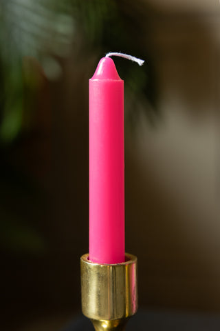 The Hot Pink Short Dinner Candle shown in a gold candlestick holder with the wick unlit. 
