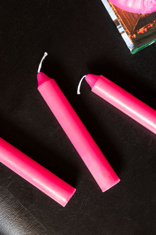 An image showing 3 of the Hot Pink Short Dinner Candles on a black surface with a book in the corner.