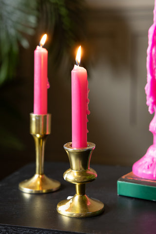A couple of the Hot Pink Short Dinner Candles shown in gold candlesticks on a black console table.