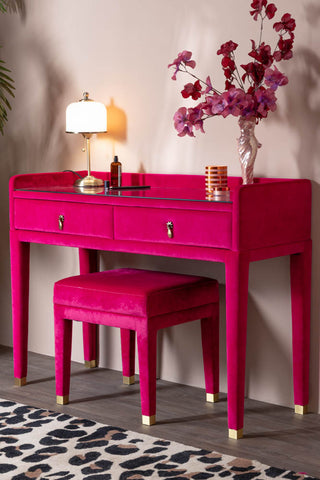 The Hot Pink Velvet Dressing Table & Stool shown with a leopard rug, pink blossom flowers and a vintage-style table lamp styled on top. 