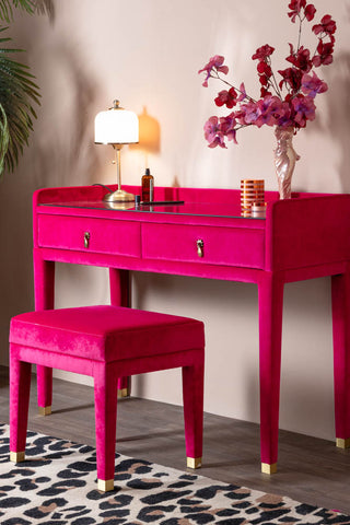 The Hot Pink Velvet Dressing Table & Stool shown with the stool out and pretty styling, including pink flowers, a leopard rug and a vintage-style table lamp. 