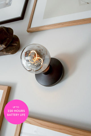 The Humble - Wall Light Cable-Free Mood Lighting in Black & Smoked Glass Shade displayed on a wall with various frames.