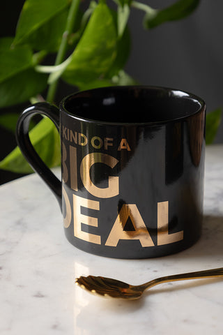 The I'm Kind Of A Big Deal Mug seen from an angle, displayed on a marble surface with a spoon and a plant in the background.