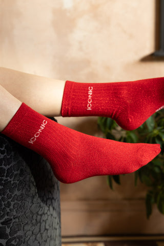 The Iconic Red Glitter Socks shown worn by a model against a plaster wall. 