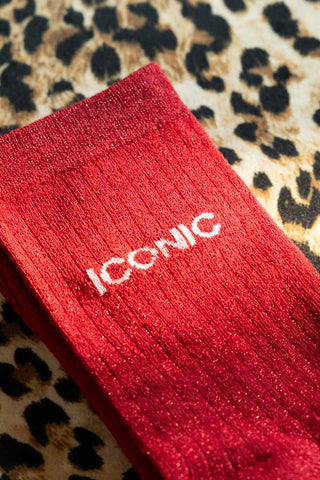 The Iconic Red Glitter Socks shown against a leopard background. The socks are red with the word 'iconic' in white. 