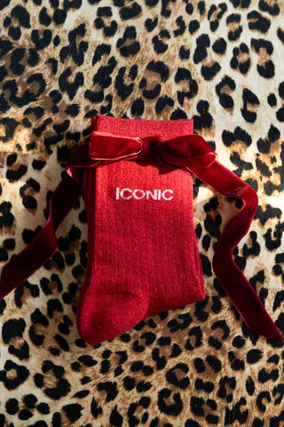 The Iconic Red Glitter Socks shown with a red bow against a leopard print background. 