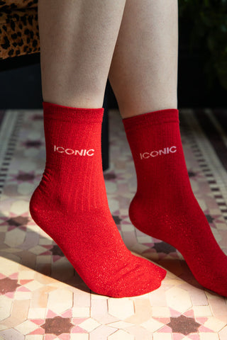 The Iconic Red Glitter Socks shown on a model against a pink star tile-effect floor. 