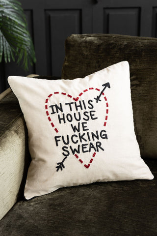 The In This House We Swear Embroidered Cushion styled on a velvet sofa with a plant in the background.