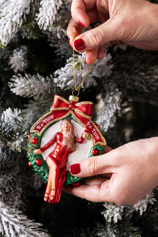 A christmas tree decoration being placed onto the branch of a christmas tree.